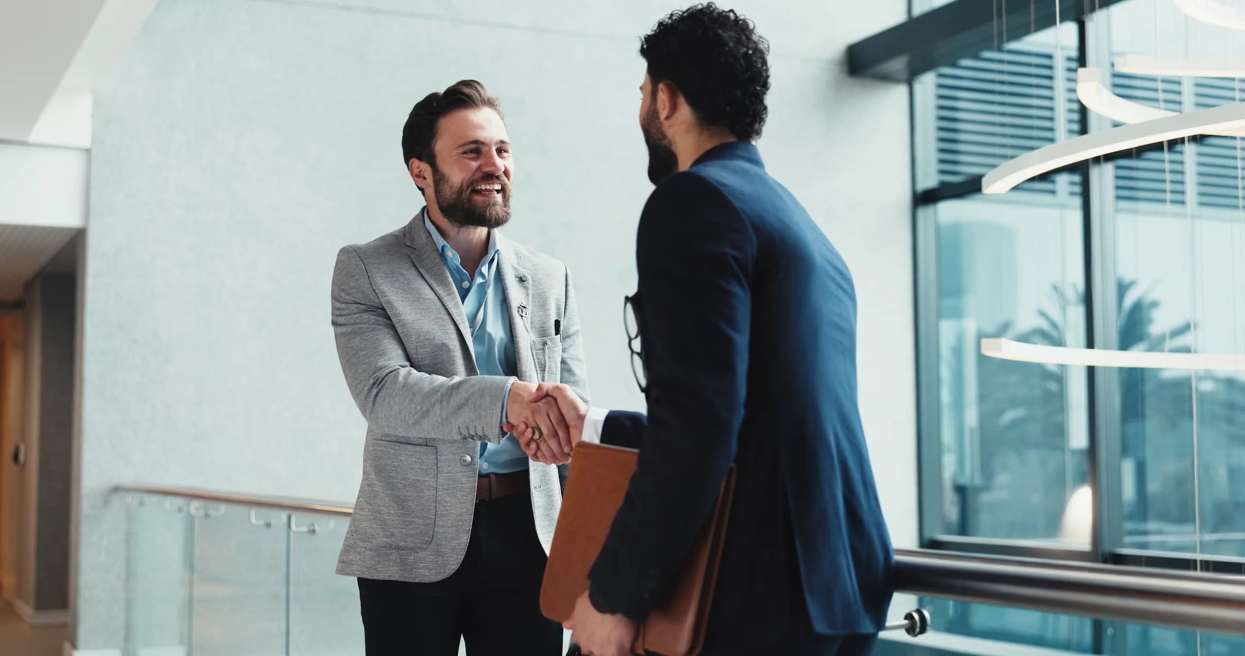 Zwei Männer im Business-Outfit schütteln sich im Gebäude die Hände.