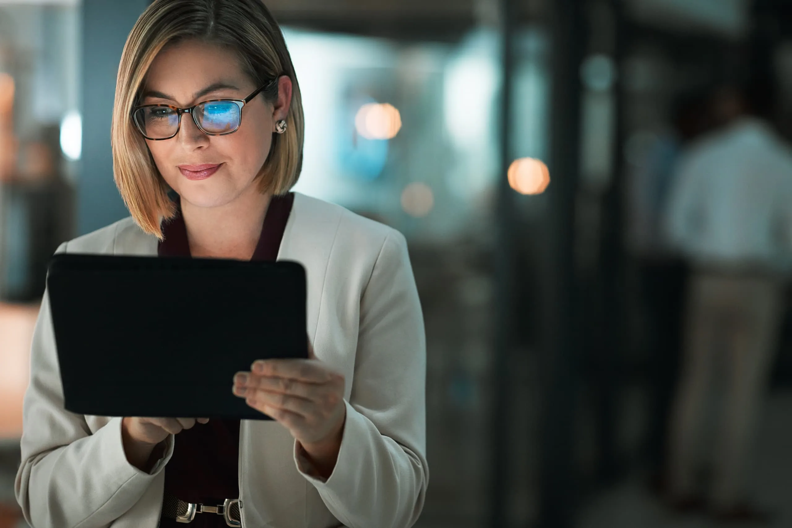 Eine Geschäftsfrau mit Brille blickt auf ein Tablet, das sie in den Händen hält. Sie nutzt das Internet für ihre Arbeit.